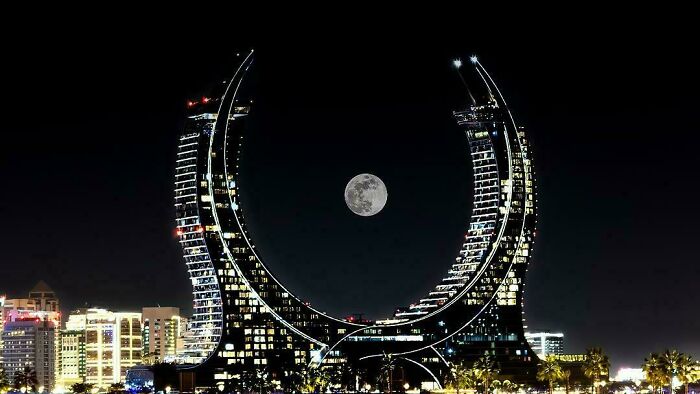 Two crescent-shaped buildings framing a full moon at night, perfect buildings for an evil mastermind.