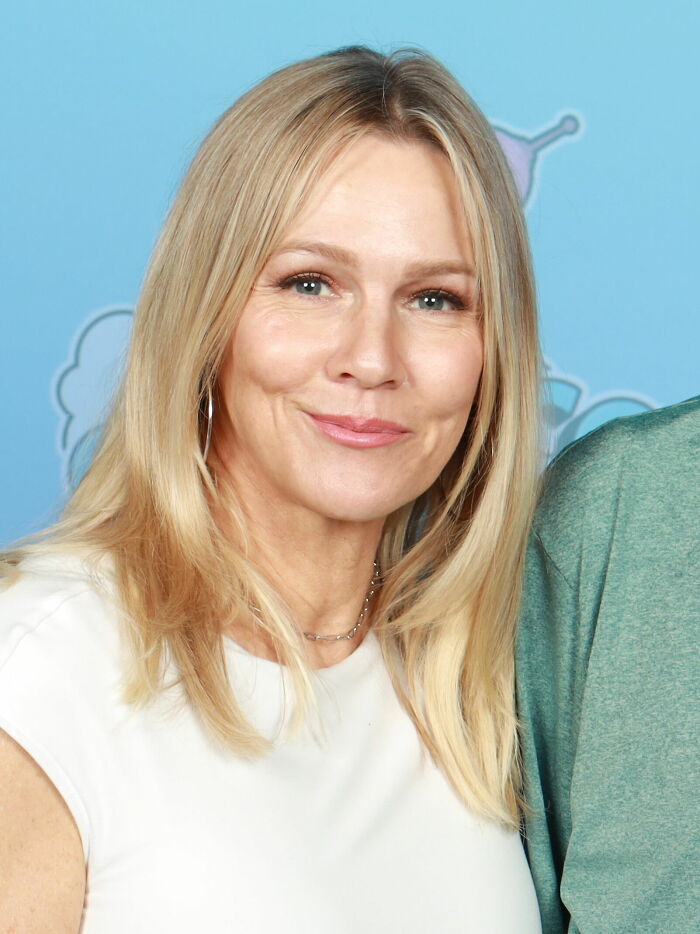 Jennie Garth smiling with blonde hair, wearing a white top, highlighting her bio and career in entertainment industry.