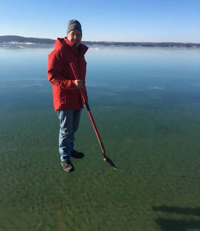 Man appearing to stand on clear frozen lake holding a shovel in an unedited photo that might mess with your brain.