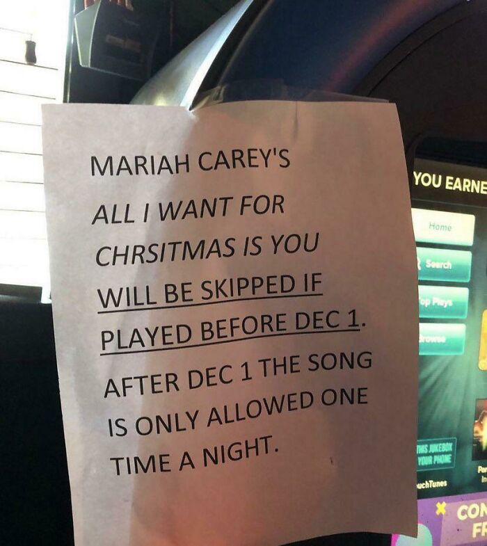 A paper sign with oddly specific rules for playing Mariah Carey's Christmas song, limiting plays before and after December 1.