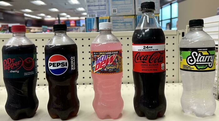 Five different soda bottles lined up on a store counter, displaying brand variety and creative packaging designs.