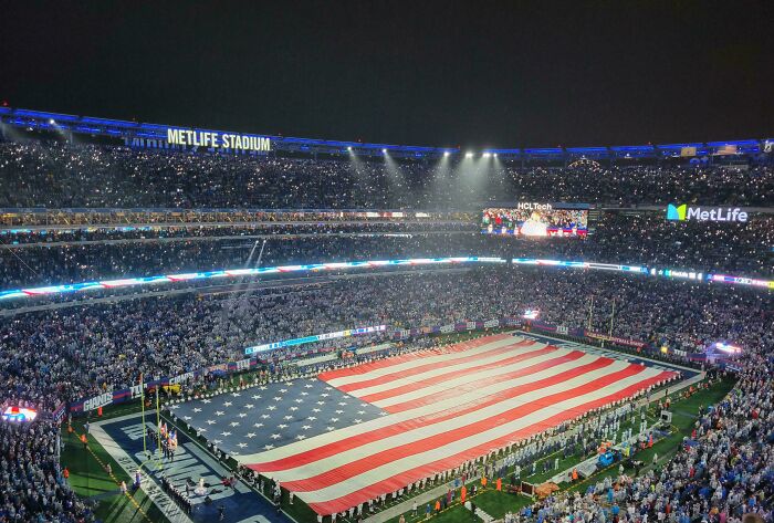 Large crowd at MetLife Stadium holding a giant American flag, showcasing intelligence in creative public displays.