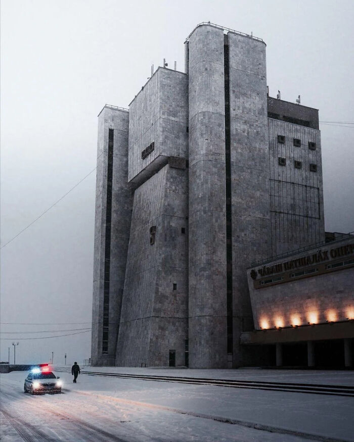 Bleak urban hell brutalist building in snow with police car and lone figure