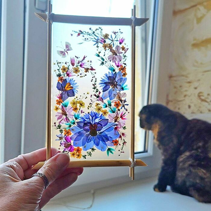 A person holding a handmade project of pressed flowers in a wooden frame. Looks like it took talent and patience.
