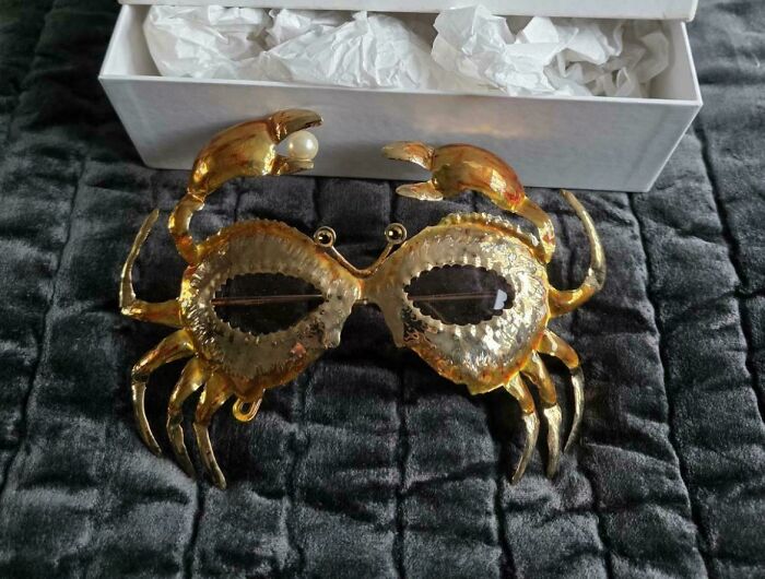 A golden crab-shaped mask with pearls for eyes, resting on a gray blanket, a fantastic thrift store jackpot.