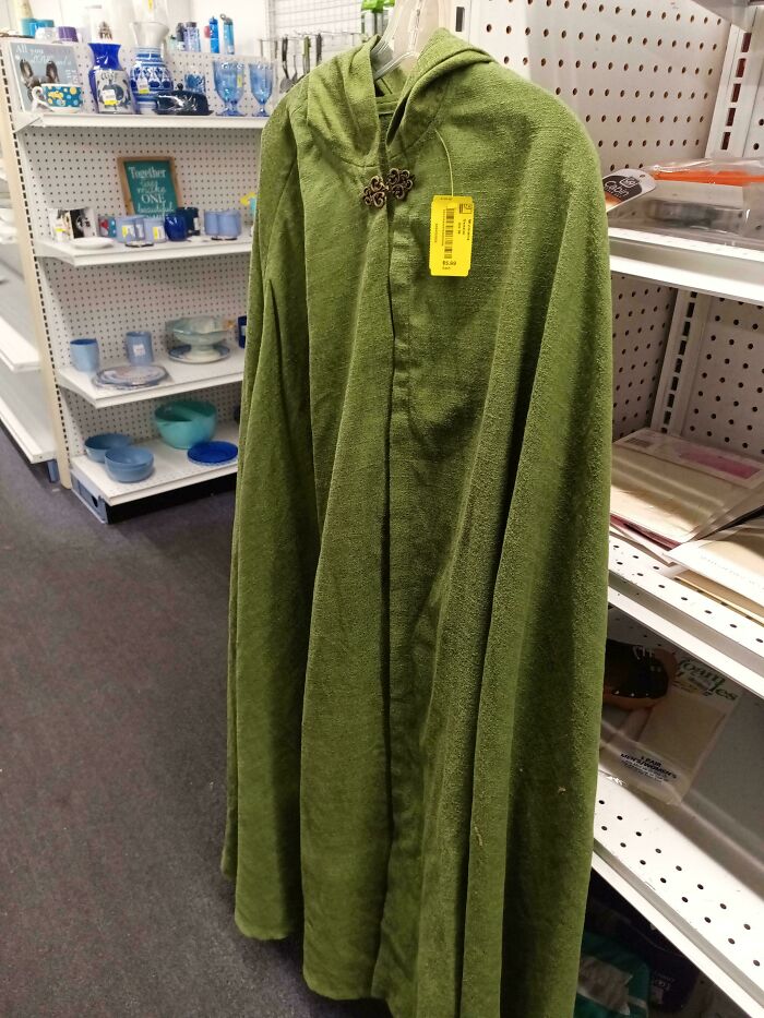 A vibrant green hooded cape with a decorative clasp, hanging in a thrift store aisle, an exciting jackpot discovery.