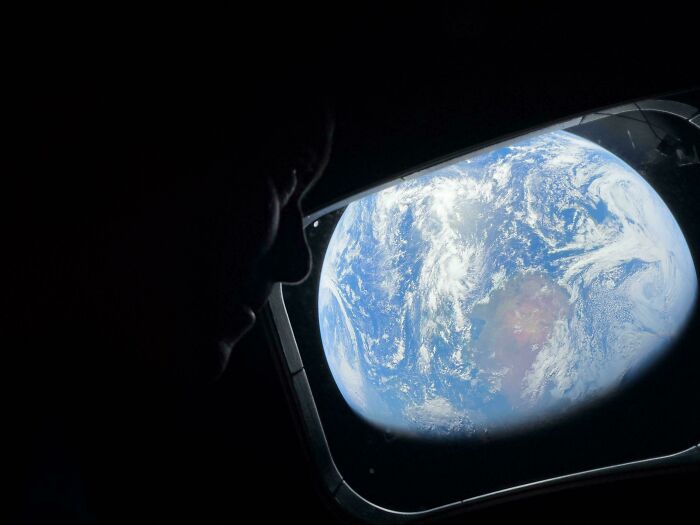 A person in profile gazing out a window at a view of planet Earth, an interesting post for an Aussie.