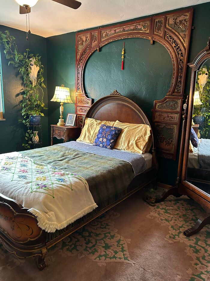 A unique thrift store bedroom with a dark green wall, antique wooden headboard, and a large mirror, showing a great jackpot find.