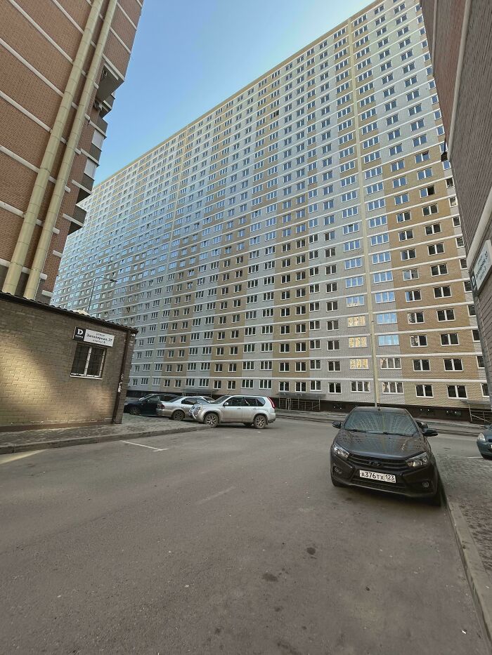 Large grey residential building towering over empty urban street with parked cars