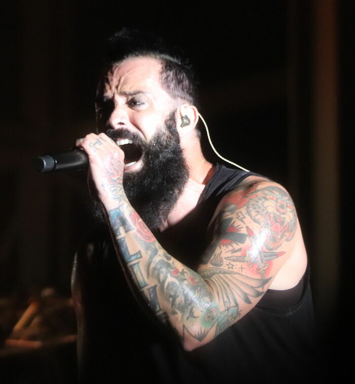 John Cooper performing on stage with tattoos and a beard, showcasing energy and passion in his career highlights.