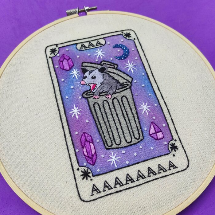 A unique embroidery creation of a possum in a trash can on a tarot-like card, inspiring new hobbies.