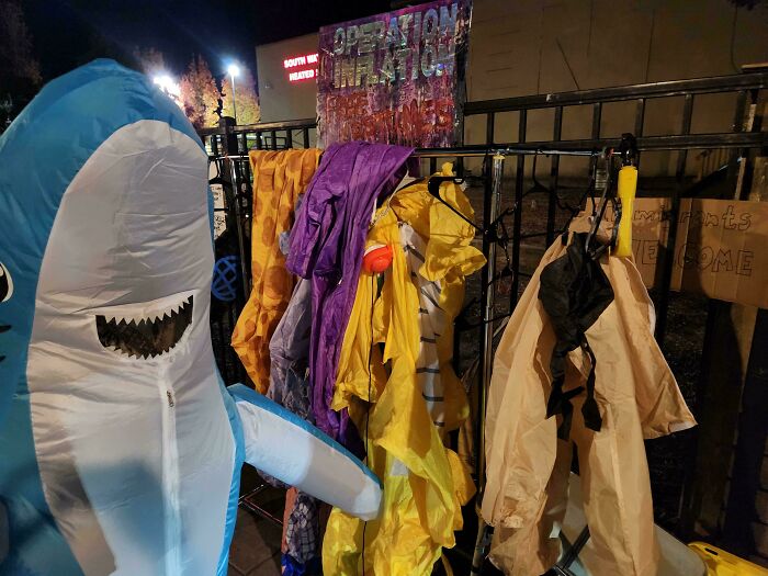 Person wearing inflatable shark costume posing next to colorful outfits, capturing the essence of states in the US.