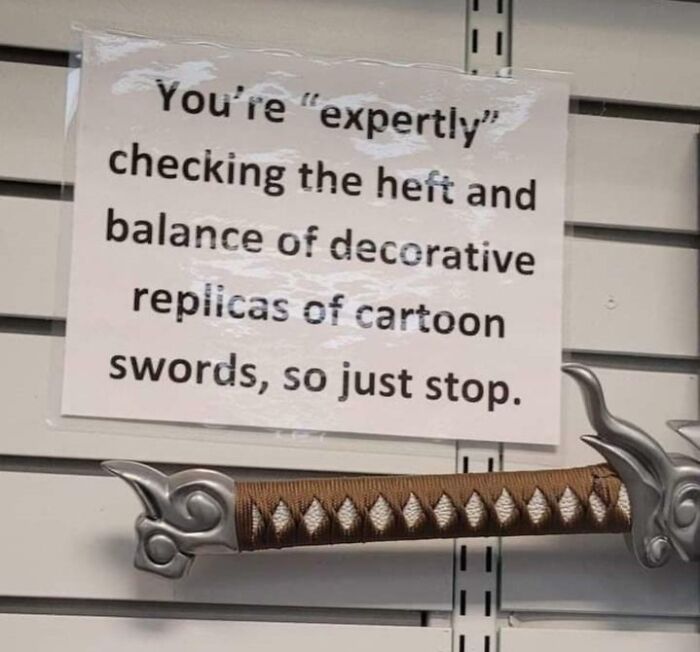 A sign with an oddly specific rule: "You're 'expertly' checking the heft and balance of decorative replicas of cartoon swords, so just stop."