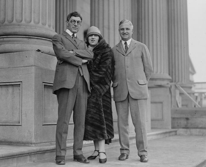 Three people in vintage attire posing outside a classical building in a rare and interesting photo from a past era.