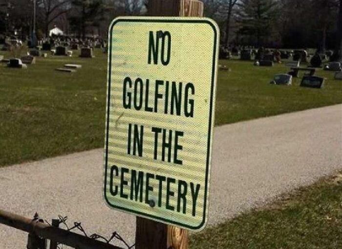 A yellow sign in a cemetery reads "NO GOLFING IN THE CEMETERY." An oddly specific rule.