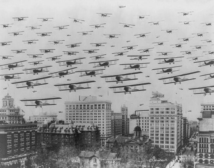 Large formation of vintage biplanes flying over a cityscape, a rare and interesting photo from a past time.