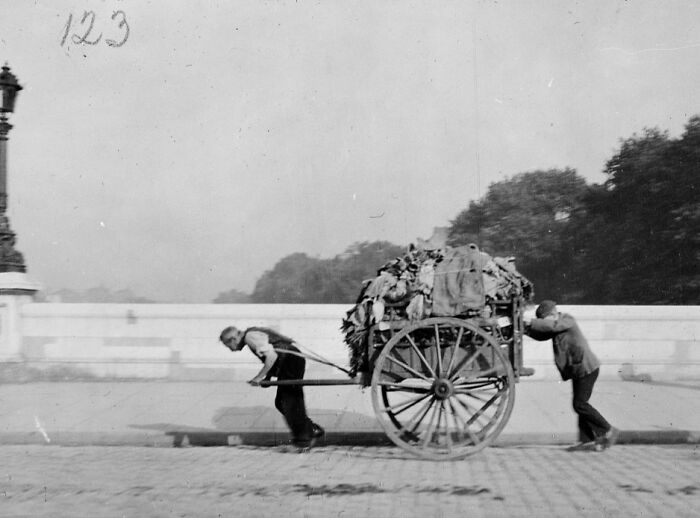 Black and white photo of two men transporting a heavy cart loaded with materials from a time we will never experience.