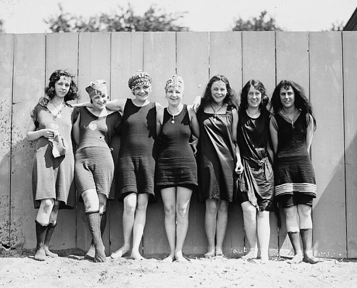 Group of young women in vintage swimsuits posing by a wooden fence in a rare and interesting photo from history.