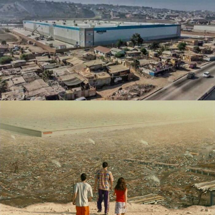 A large warehouse overshadowing a sprawling slum area with people observing the vast contrast highlighting modern stupidity.