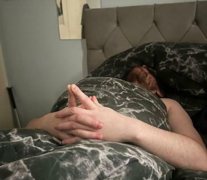 Person caught sleeping in a bed with hands resting on a patterned blanket, showing a hilarious and unhinged sleeping position.