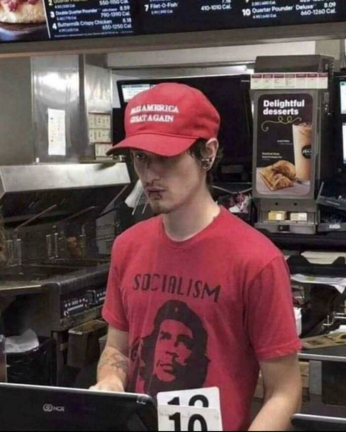 Young man wearing a MAGA hat and socialism t-shirt working behind a fast food counter, illustrating confusing modern times.
