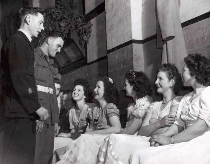 Group of smiling young women in vintage dresses talking with two men in military uniforms, rare and interesting photo from past.