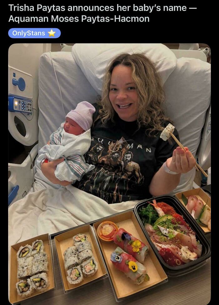 New mother in hospital bed holding newborn baby with sushi trays, highlighting depressing posts about living in the stupidest time.