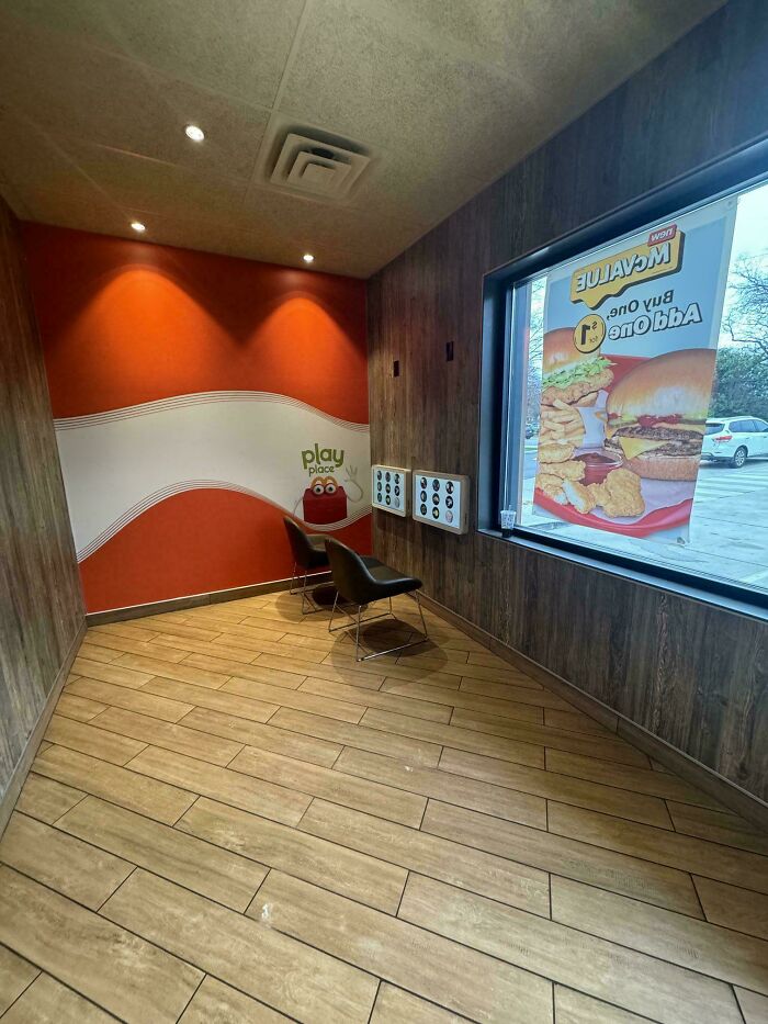 Empty fast food play place with two chairs near wall panels and a window showing a food advertisement reflecting stupidest time in history.