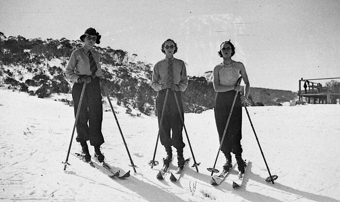 Three women skiing in vintage attire on a snowy slope, showcasing rare and interesting photos from a historical time.