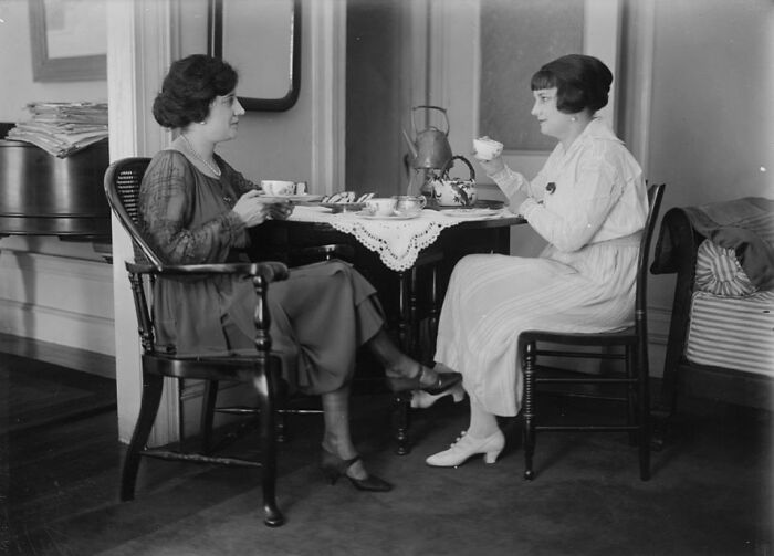 Two women dressed in vintage clothing enjoying tea at a table in a rare and interesting historical photo.