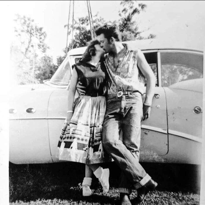 Couple from decades ago sharing a kiss beside a vintage car, capturing moments that still speak louder than today’s headlines.