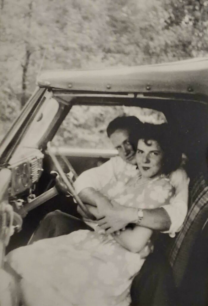 Vintage black and white photo of a couple embracing inside a car, showcasing timeless moments from decades ago.