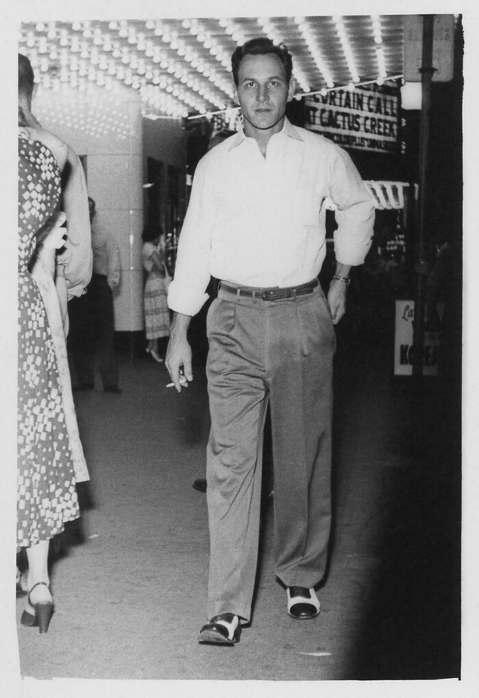 Black and white photo of a man walking on a sidewalk from decades ago, capturing vintage style and timeless mood.