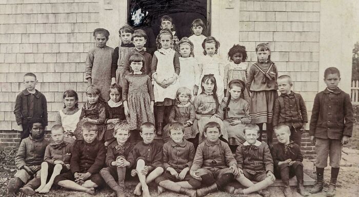 Group of children posing outside a vintage school building in a black and white photo from decades ago.