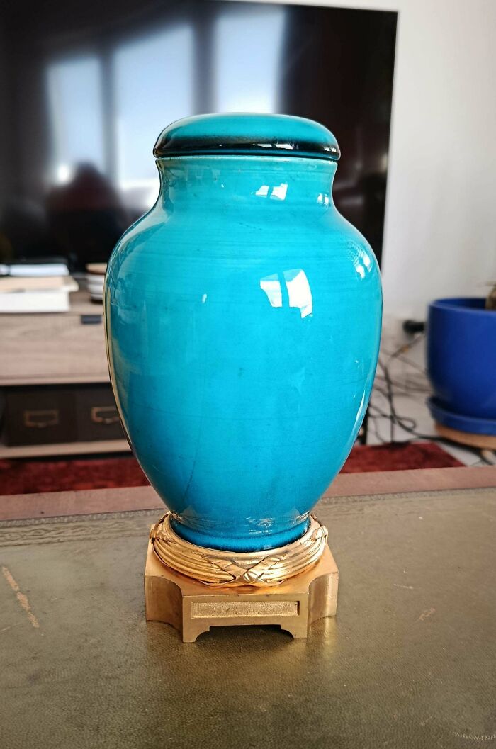 A beautiful turquoise antique vase with a lid, sitting on a golden, ornate base.