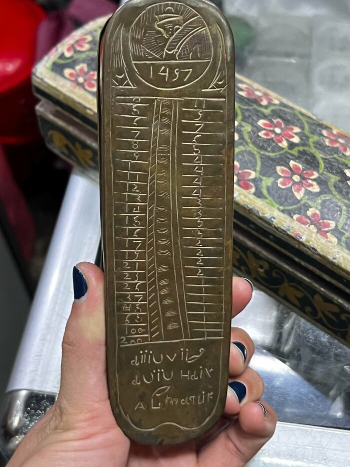 A hand holding a brass ruler-like antique with etched numbers and text, revealing remarkable historical details.