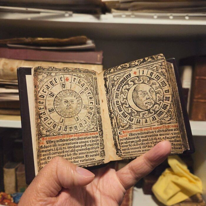 A hand holding open a small, remarkable antique book with illustrations of the sun and moon, a truly special discovery.