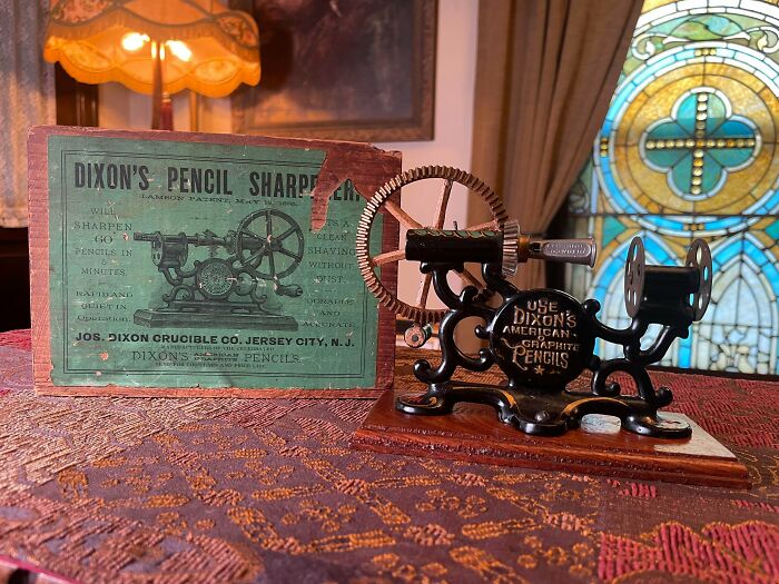A remarkable antique Dixon's pencil sharpener and its original box, displayed on a patterned tablecloth.
