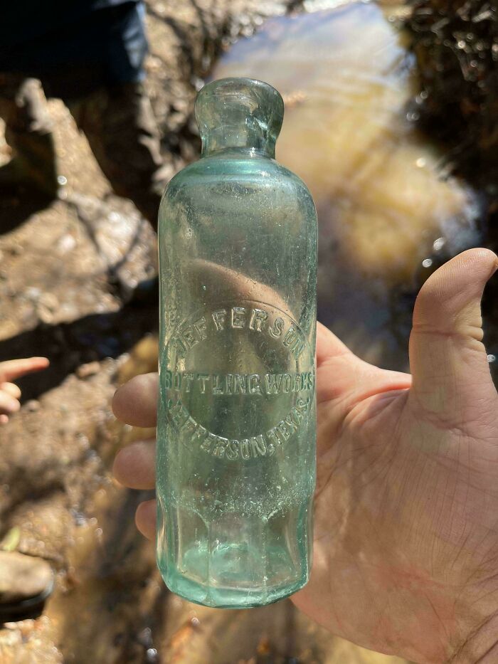 A hand holding a remarkable antique Jefferson Bottling Works bottle found near water.