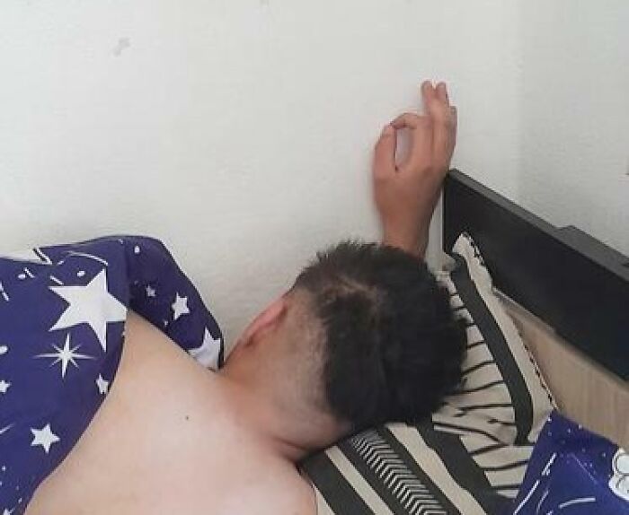 Person caught sleeping in an unhinged way with arm awkwardly bent against the wall on a patterned pillow.