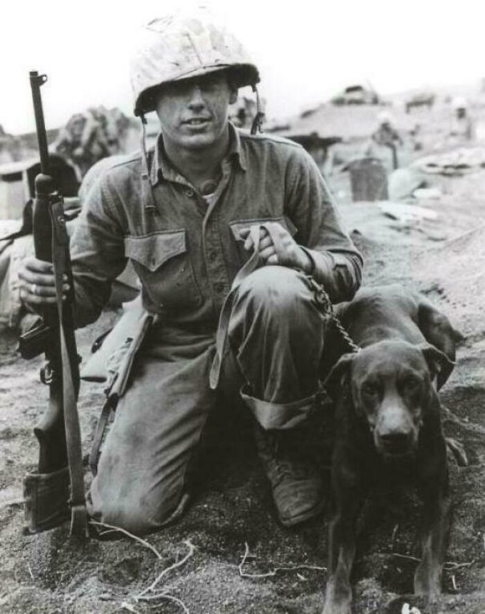 A soldier kneeling with his dog and a rifle, an emotional historical photo of companionship during conflict.