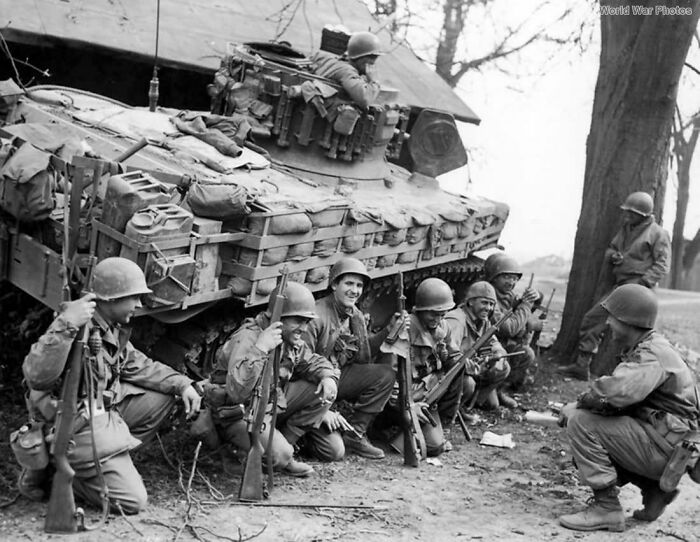 Soldiers with rifles posing next to a tank, representing an emotional historical photo.