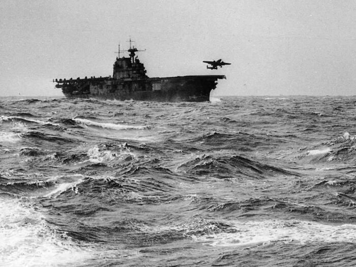 An aircraft carrier at sea with a plane taking off, a powerful image among historical photos.