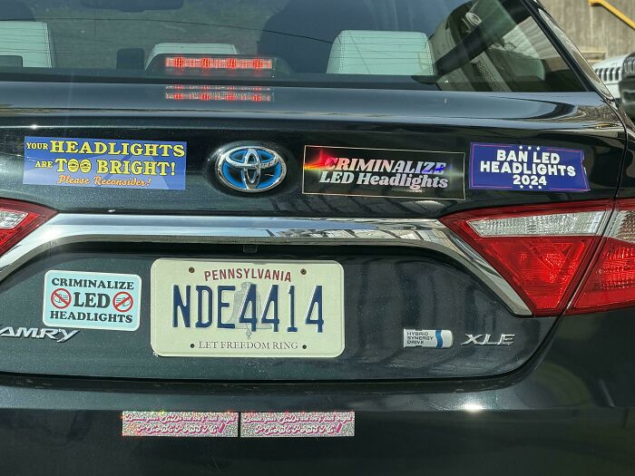 Multiple unfiltered bumper stickers on a black car, including "Criminalize LED Headlights".