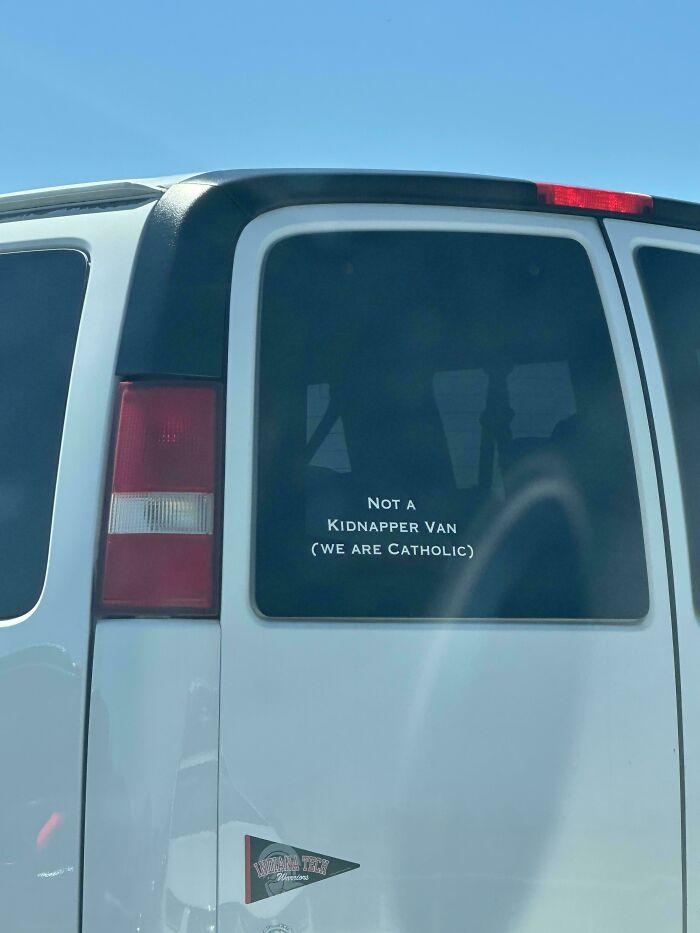 A white van features a funny bumper sticker on its back window, Not a kidnapper van (we are Catholic), a truly unfiltered bumper sticker.