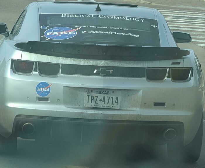 A car with unfiltered bumper stickers on the back window and bumper, including NASA IS FAKE and LIES.