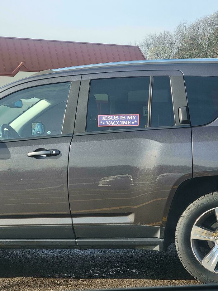 A car with an unfiltered bumper sticker on the window that says, JESUS IS MY VACCINE.