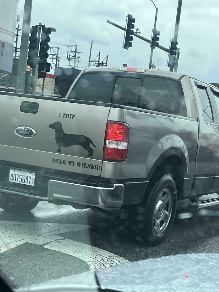 A funny bumper sticker on a truck that reads, I TRIP OVER MY WIENER, with a dachshund silhouette.