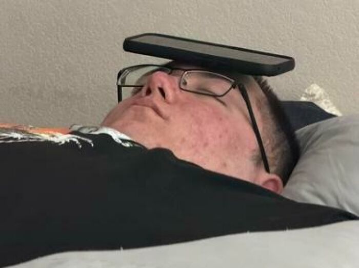 Person caught sleeping with glasses and a phone balanced on their face in a hilarious and unhinged way.