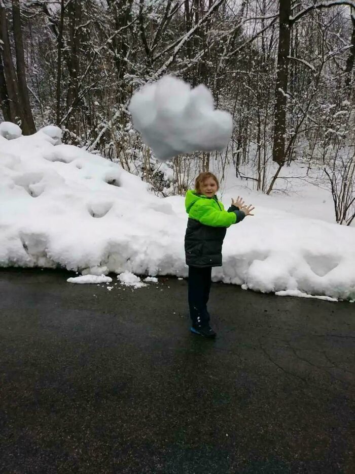 Child in a green jacket appears to levitate a snowball in a snowy outdoor setting, creating a misleading and confusing photo effect.